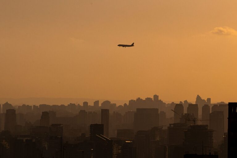 A silhouette of an airplane flying over Sao Paulo's skyline during a golden sunset.