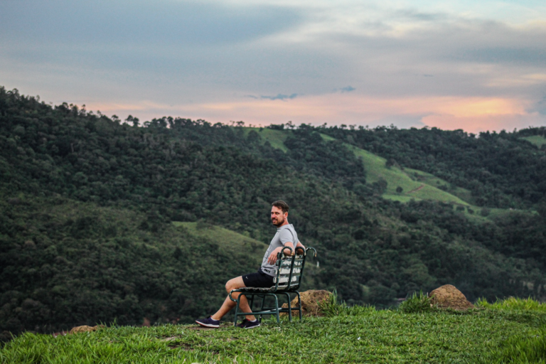A man sits on a bench enjoying a serene view of a lush green valley at sunset.