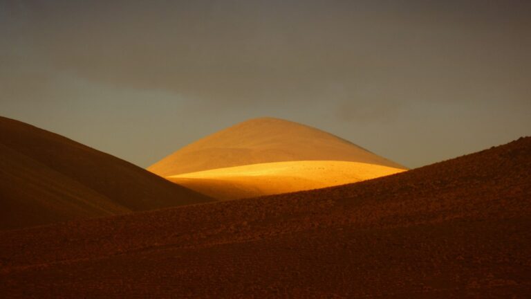 Serene landscape of sunlit desert hills under a dramatic sky at sunset.